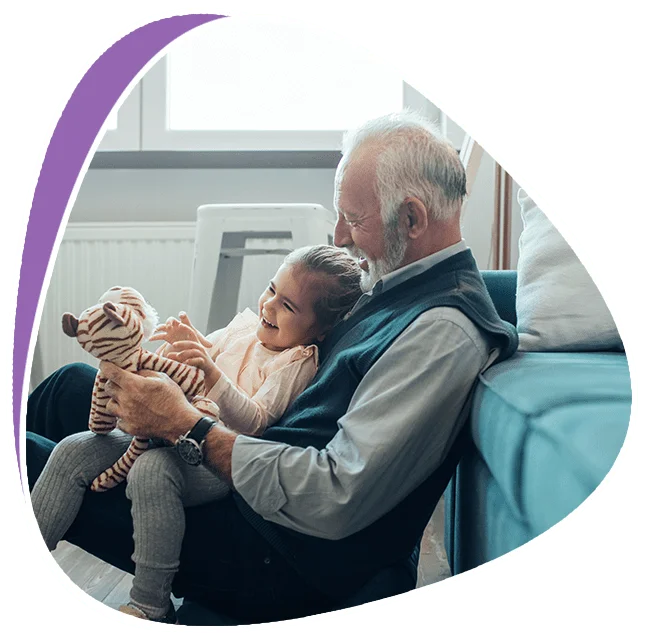 A child sits on her grandparent's lap, happily playing with a stuffed tiger.