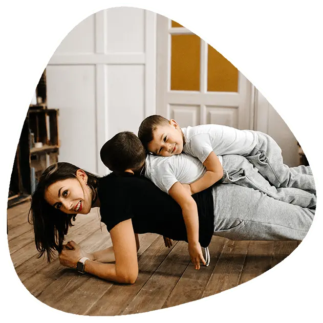 A mother is doing a plank with two children lying on her back.