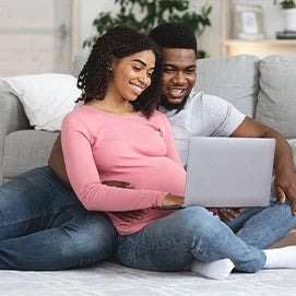 A pregnant couple looking at a laptop screen.